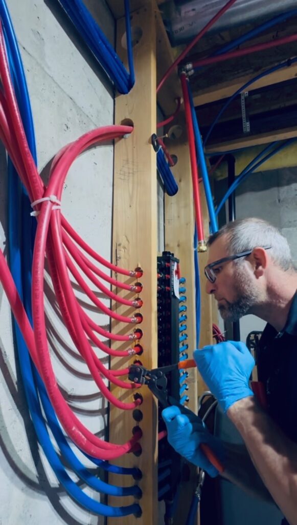 Plumber crimping PEX water supply lines at a manifold during a pipe repair